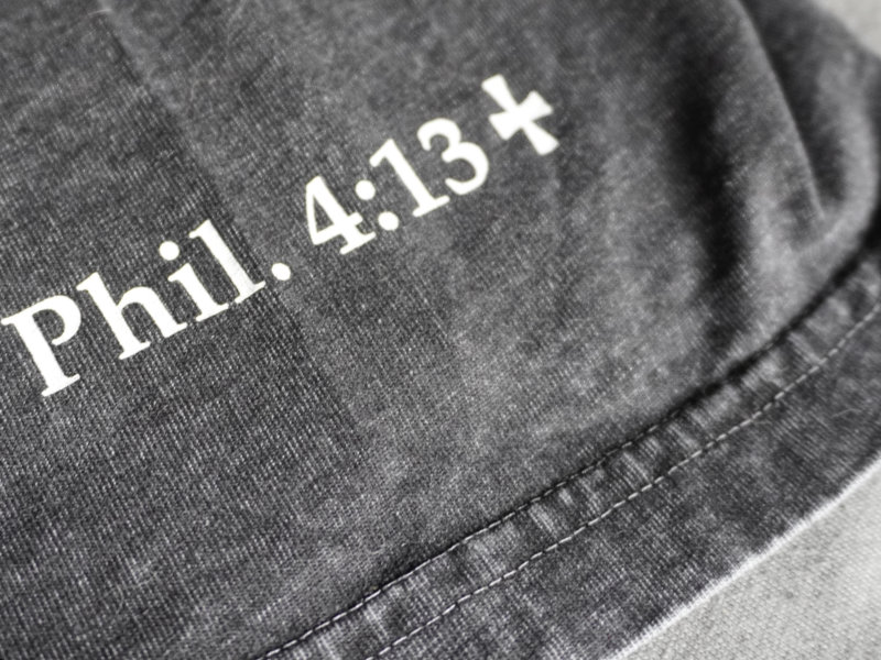 Close-up of the sleeve hem and Philippians 4:13 detail on the acid wash black tee.